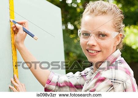 Stock Photography - Woman measuring plywood and marking with pencil. Fotosearch
