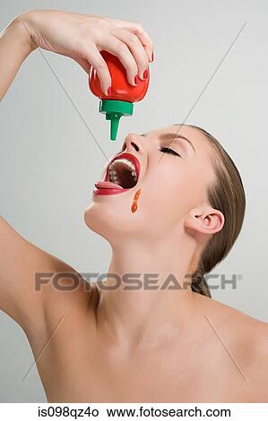 Picture - Woman pouring tomato ketchup in her mouth. Fotosearch