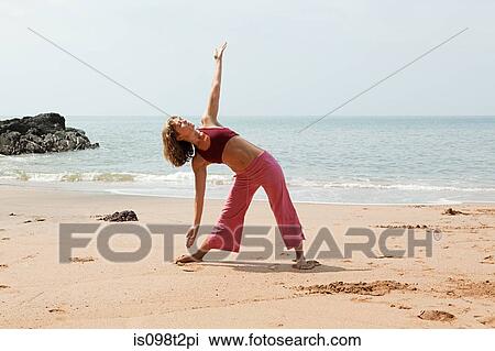 Stock Image - Woman practicing yoga on a beach. Fotosearch