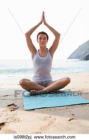 Stock Image - Woman practicing yoga on a beach. Fotosearch