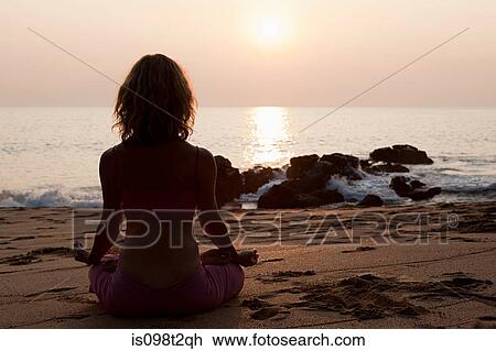 Stock Image - Woman practicing yoga on beach at sunset. Fotosearch
