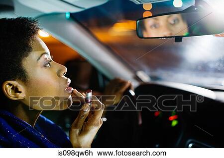 Stock Image - Woman putting on lipstick in car. Fotosearch
