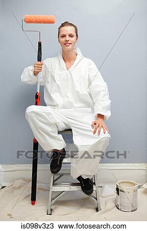 Stock Image - Woman sitting on stepladders with paint roller, portrait. Fotosearch