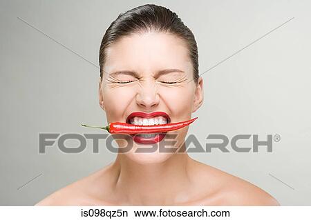 Picture - Woman with a red chili pepper in her mouth. Fotosearch