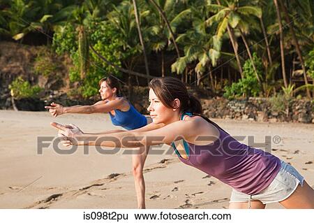 Stock Photograph - Women practicing yoga on a beach. Fotosearch