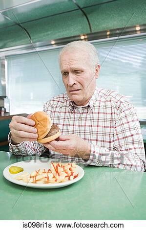 Stock Photograph - Worried old man looking at a burger. Fotosearch