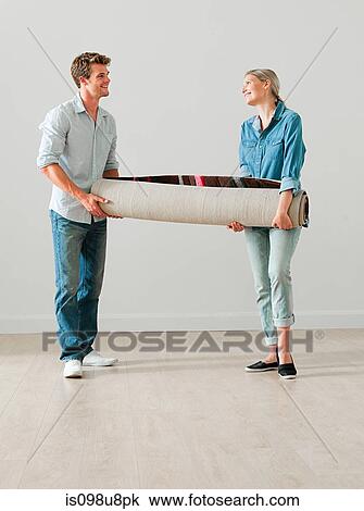 Stock Image - Young couple carrying a rolled up rug. Fotosearch