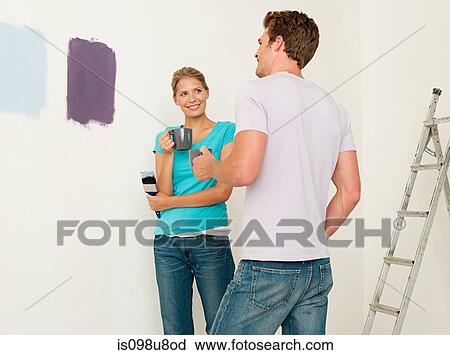 Young couple looking at paint on wall View Large Photo Image Stock Image - Young couple looking at paint on wall. Fotosearch
