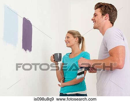 Stock Photo - Young couple looking at paint on wall. Fotosearch