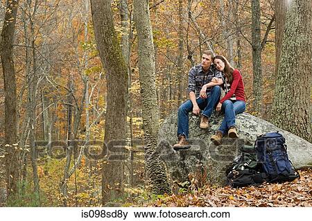 Stock Photo - Young couple sitting on boulder in forest. Fotosearch