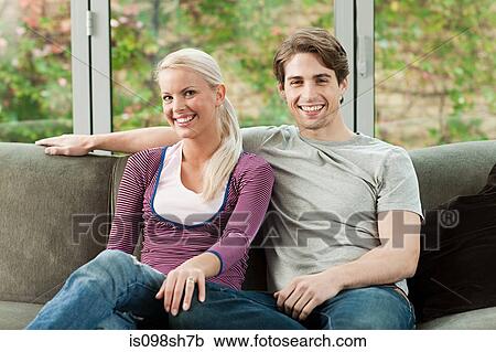 Young couple sitting on sofa at home View Large Photo Image Stock Image - Young couple sitting on sofa at home. Fotosearch