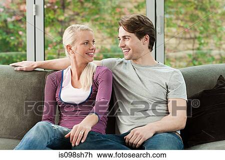 Stock Image - Young couple sitting on sofa at home. Fotosearch
