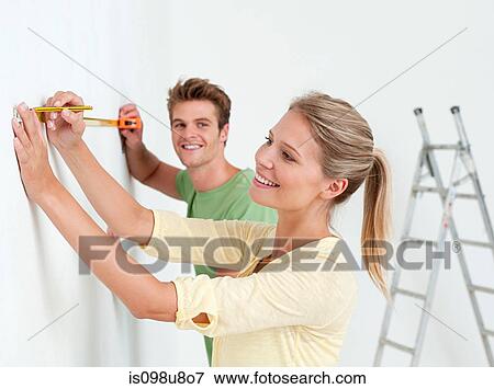 Young couple using measuring tape on wall View Large Photo Image Stock Photo - Young couple using measuring tape on wall. Fotosearch