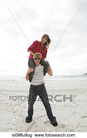 Young man carrying girl on shoulders on beach View Large Photo Image Stock Image - Young man carrying girl on shoulders on beach. Fotosearch