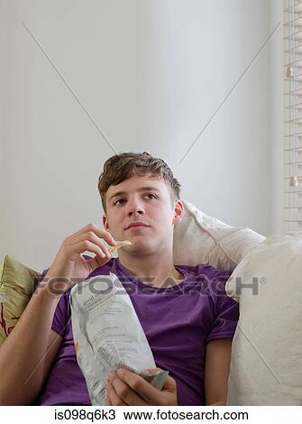Young man eating a packet of crisps View Large Photo Image Stock Image - Young man eating a packet of crisps. Fotosearch
