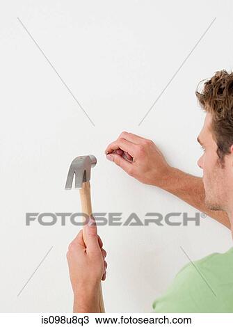 Young man hammering nail into wall View Large Photo Image Stock Image - Young man hammering nail into wall. Fotosearch