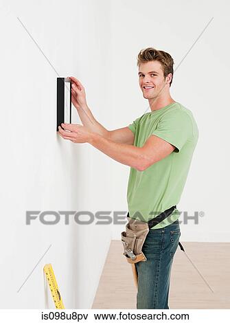 Young man hanging picture on wall View Large Photo Image Stock Photo - Young man hanging picture on wall. Fotosearch