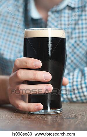 Stock Image - Young man holding pint glass, close up. Fotosearch