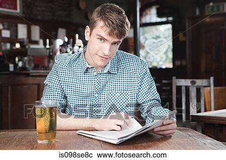Stock Image - Young man in bar with newspaper and beer. Fotosearch