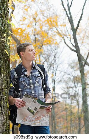 Stock Image - Young man in forest with map. Fotosearch