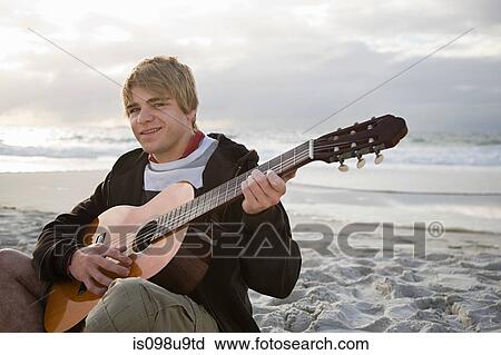 Stock Image - Young man playing guitar on beach. Fotosearch