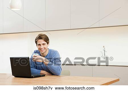 Stock Photo - Young man sitting at table with laptop. Fotosearch