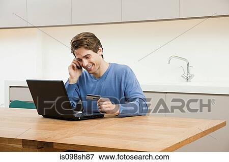 Young man sitting at table with laptop View Large Photo Image Stock Photo - Young man sitting at table with laptop. Fotosearch