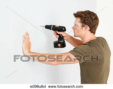 Stock Image - Young man using electric drill. Fotosearch