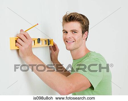 Stock Image - Young man using spirit level on wall. Fotosearch