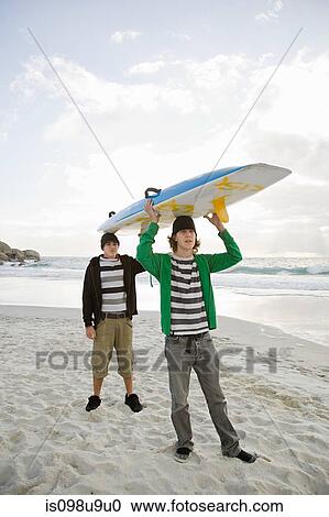 Young men carrying surfboard on head View Large Photo Image Stock Image - Young men carrying surfboard on head. Fotosearch