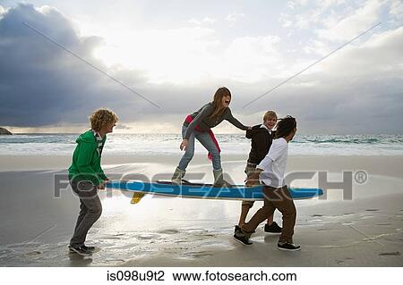 Stock Image - Young people carrying surfboard, person balancing on top. Fotosearch