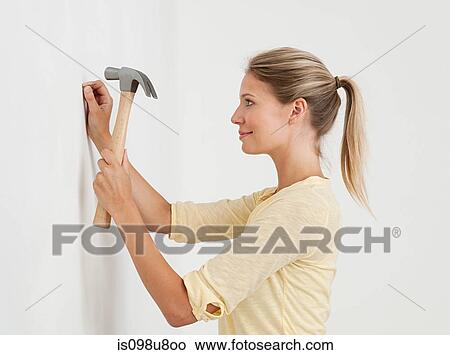 Young woman hammering nail into wall View Large Photo Image Picture - Young woman hammering nail into wall. Fotosearch