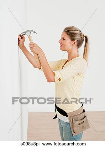 Young woman hammering nail into wall View Large Photo Image Stock Image - Young woman hammering nail into wall. Fotosearch