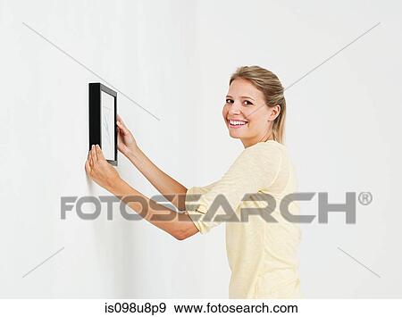 Young woman hanging picture on wall View Large Photo Image Stock Photo - Young woman hanging picture on wall. Fotosearch