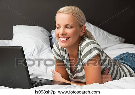 Young woman lying on bed with laptop View Large Photo Image Stock Photography - Young woman lying on bed with laptop. Fotosearch