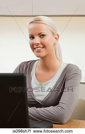 Stock Image - Young woman sitting at table with laptop. Fotosearch