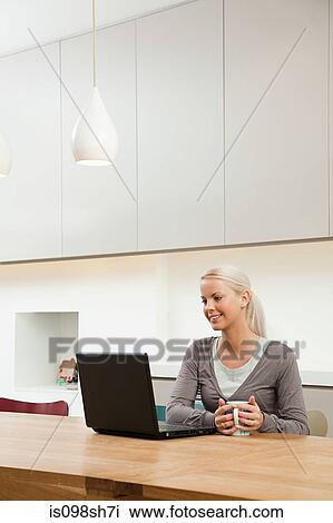 Young woman sitting at table with laptop View Large Photo Image Stock Image - Young woman sitting at table with laptop. Fotosearch