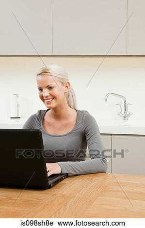 Young woman sitting at table with laptop View Large Photo Image Stock Image - Young woman sitting at table with laptop. Fotosearch