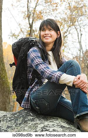 Stock Image - Young woman sitting on boulder. Fotosearch