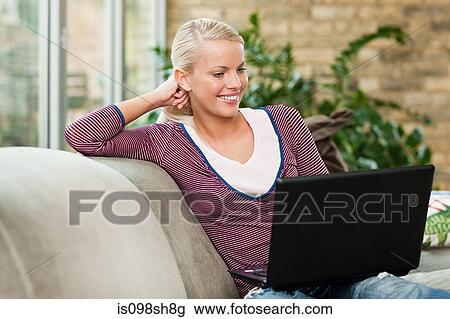Young woman sitting on sofa with laptop View Large Photo Image Stock Image - Young woman sitting on sofa with laptop. Fotosearch