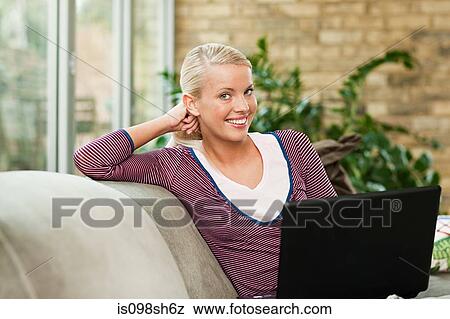Young woman sitting on sofa with laptop View Large Photo Image Stock Photo - Young woman sitting on sofa with laptop. Fotosearch