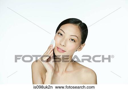 Picture - Young woman using cotton pad on face. Fotosearch