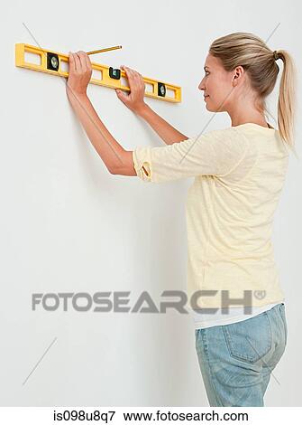 Stock Photo - Young woman using spirit level on wall. Fotosearch