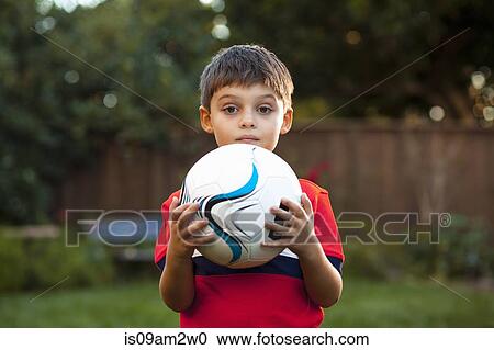 Stock Image - Boy holding football against chest in garden. Fotosearch