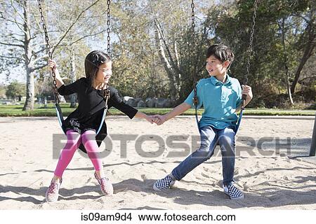 Picture - Brother and sister holding hands on playground swings in park. Fotosearch