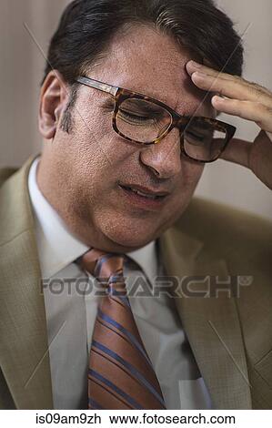 Stock Image - Close up of mature businessman with eyes closed and hand on forehead. Fotosearch