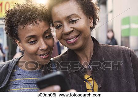 Stock Image - Close up of two mature female friends reading smartphone texts on street. Fotosearch