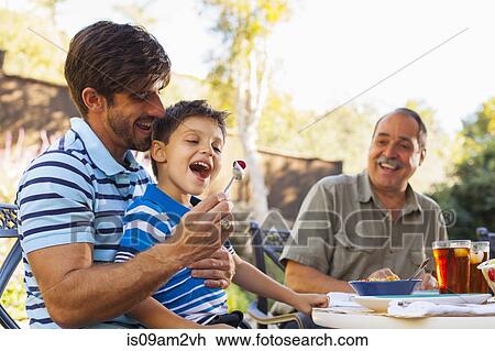 "Father feeding son on lap, grandfather in background" View Large Photo Image Stock Image - "Father feeding son on lap, grandfather in background". Fotosearch