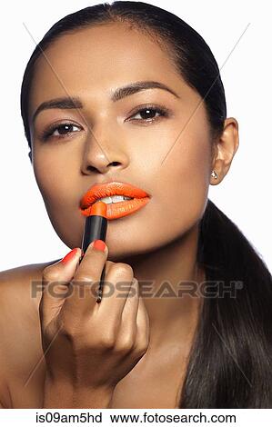 Stock Image - Female model applying orange lipstick. Fotosearch