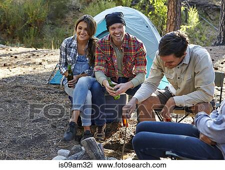 Stock Image - "Four young adult friends sitting by campfire in forest, Los Angeles, California, USA". Fotosearch